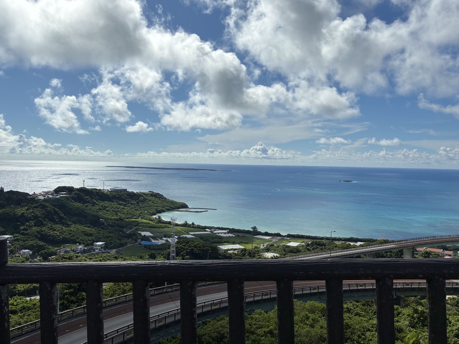 沖縄県南城市・ニライカナイ橋展望台から望む南部の絶景。青空と白い雲・エメラルドグリーンの海・緑の山々と橋が広がる夏の沖縄パノラマビュー