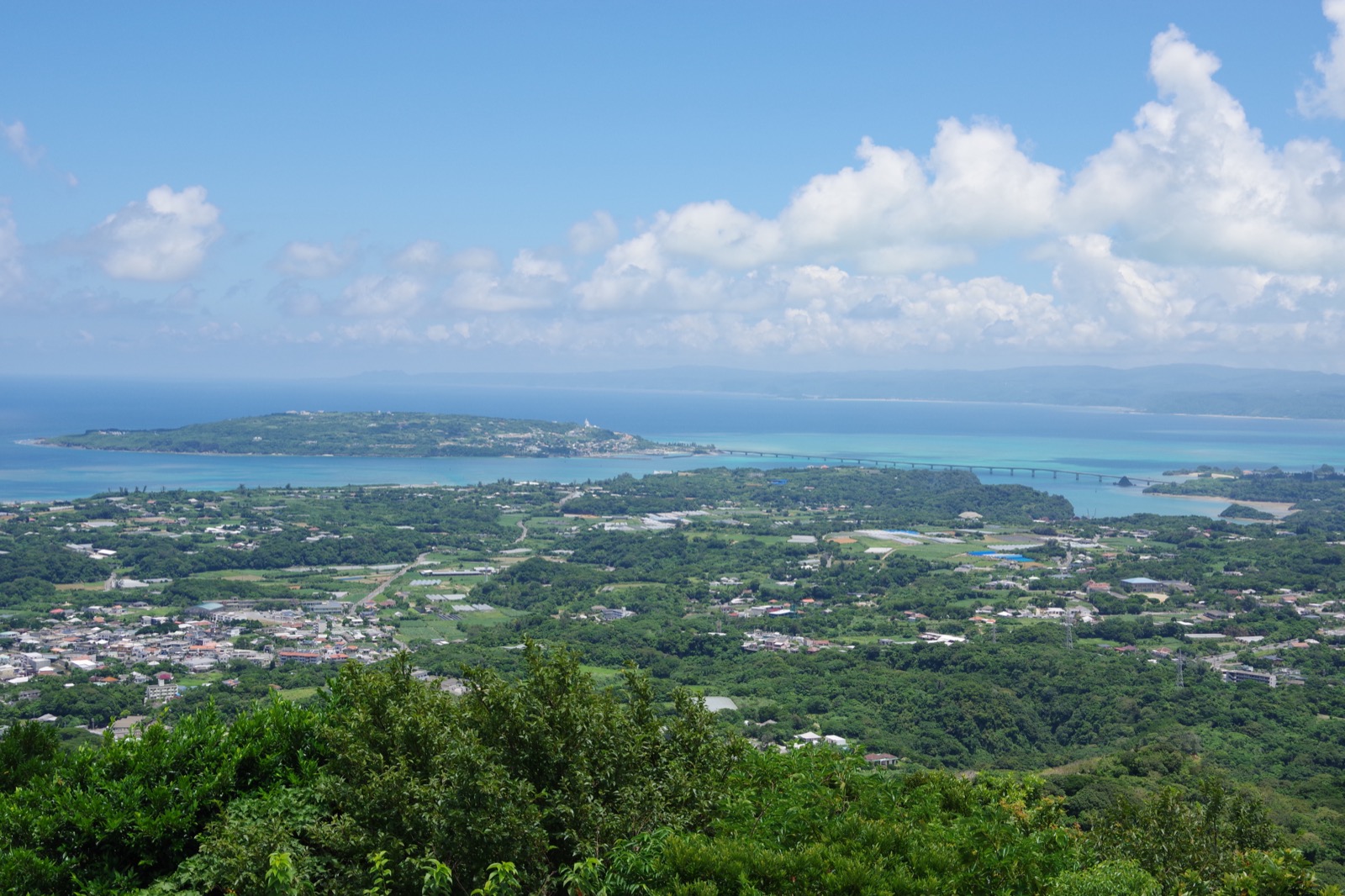 沖縄本島・今帰仁村の乙羽岳から望む古宇利島と古宇利大橋の絶景パノラマ。エメラルドグリーンの海と青空・白い雲