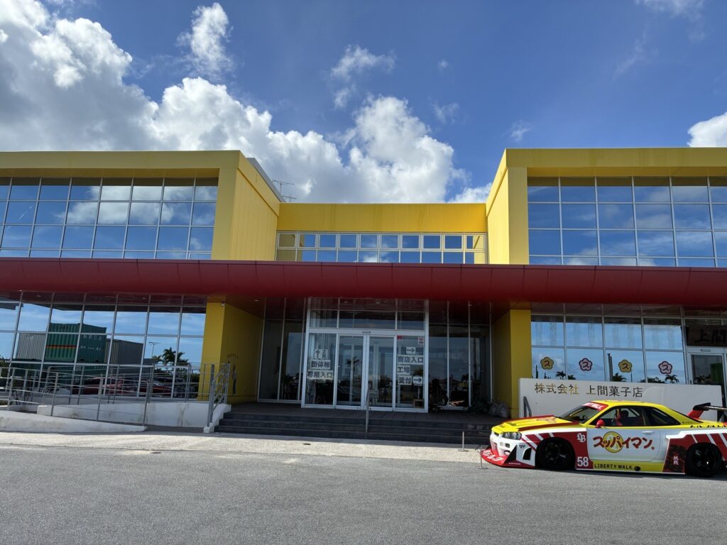 上間菓子店の本店外観。黄色い建物とスッパイマンのラッピングカー