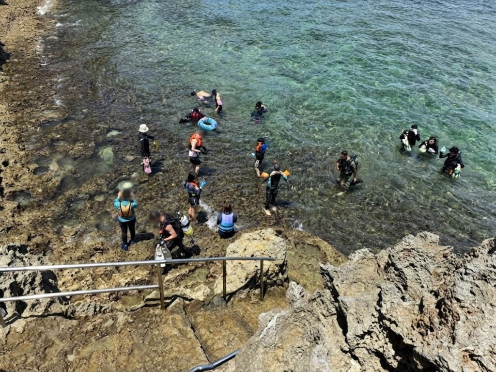 真栄田岬の入水地点。ライフジャケットや浮き輪を着けた家族連れ