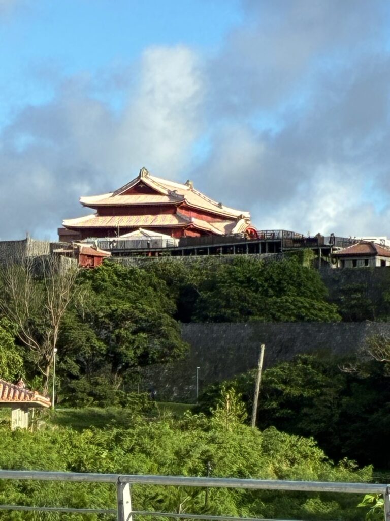 夕方の光に照らされた首里城正殿を園外から見上げた様子